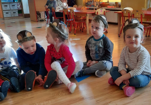 Dzieci siedzą z misiowymi uszami na głowie